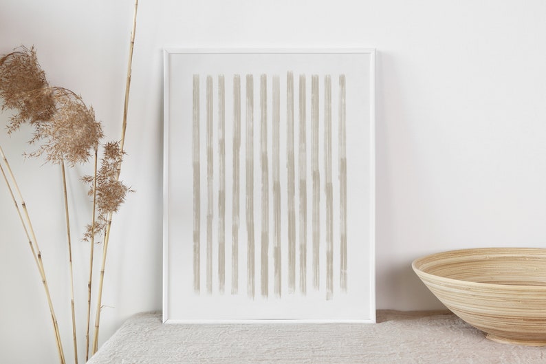 Op de afbeelding: Een ingelijst print met een minimalistisch ontwerp met een reeks verticale, lichtbruine penseelstreken op een witte achtergrond.