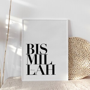 May include: A white framed print with the text "BIS MIL LAH" in black bold letters. The text is centered on the print. The print is on a white surface with a woven straw mat to the right.
