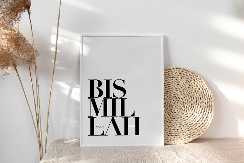 May include: A white framed print with the text "BIS MIL LAH" in black bold letters. The text is centered on the print. The print is on a white surface with a woven straw mat to the right.