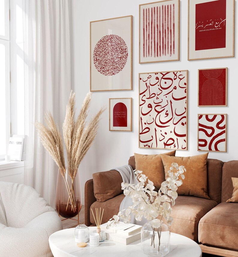 May include: A living room interior with a brown leather sofa, a white fluffy armchair, and a white coffee table. The wall is decorated with a gallery wall of framed prints featuring red Arabic calligraphy and abstract geometric designs.