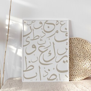 Op de afbeelding: Een ingelijst drukwerk met een witte achtergrond en beige Arabische kalligrafie. De print wordt weergegeven op een lichtbeige oppervlak met een geweven rieten mat.
