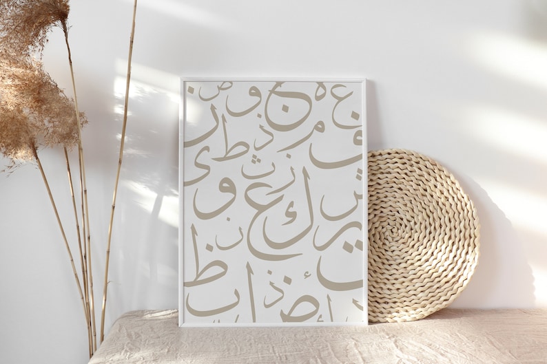 Op de afbeelding: Een ingelijst drukwerk met een witte achtergrond en beige Arabische kalligrafie. De print wordt weergegeven op een lichtbeige oppervlak met een geweven rieten mat.