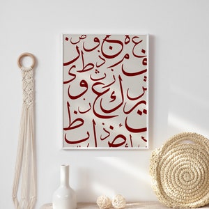 May include: A framed print with a white background and red Arabic calligraphy. The print is hanging on a white wall above a table with a white vase and a woven basket.