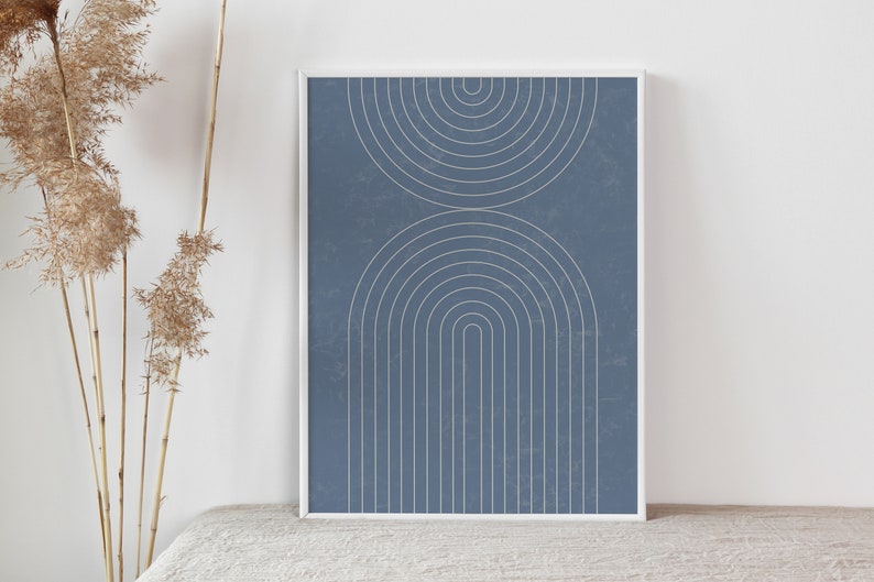 May include: Framed art print featuring a minimalist design. The artwork showcases two sets of arched lines in a light beige color against a textured, dusty blue background. The print is encased in a white frame.