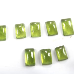 May include: Eight green rectangular gemstones, also known as peridot, are arranged in two rows on a white surface.