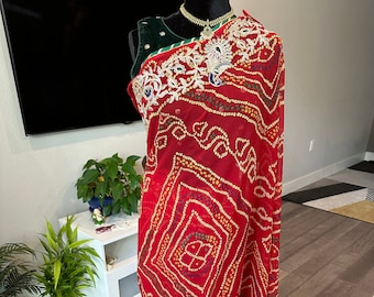 May include: A red chiffon saree with gold and white embroidery. The saree has a geometric pattern and a ruffled hem.
