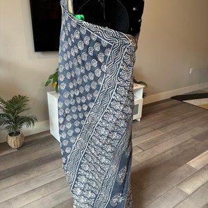 May include: A grey and white patterned sari with a gold border. The sari is draped on a mannequin.