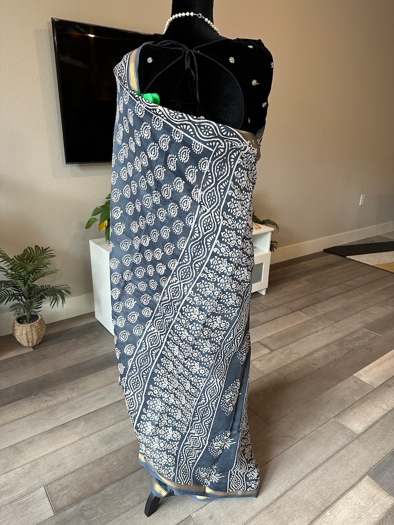May include: A grey and white patterned sari with a gold border. The sari is draped on a mannequin.