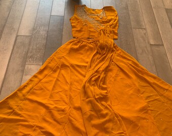 Può includere: Un completo in due pezzi color giallo senape con un top corto senza maniche e una gonna lunga. Il top presenta un design di perline argentate sul collo. La gonna ha un design drappeggiato ed è decorata con piccole perline argentate.