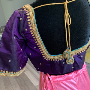 May include: A purple and pink Indian bridal blouse with gold and blue embroidery. The blouse has a deep V-neckline and a tie-up back.