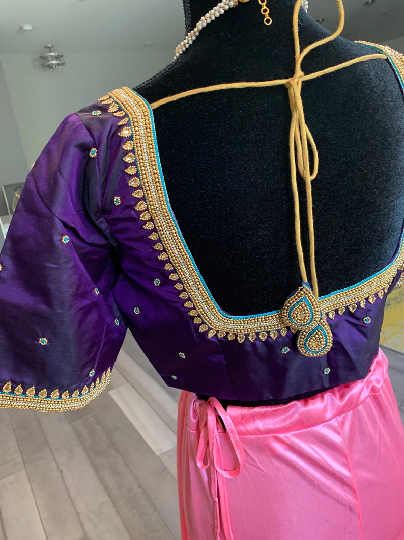 May include: A purple and pink Indian bridal blouse with gold and blue embroidery. The blouse has a deep V-neckline and a tie-up back.