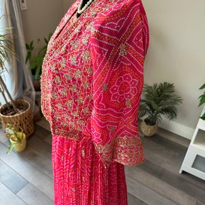 May include: A pink and white patterned dress with gold embroidery and a pearl necklace. The dress has a long skirt and a short-sleeved top.