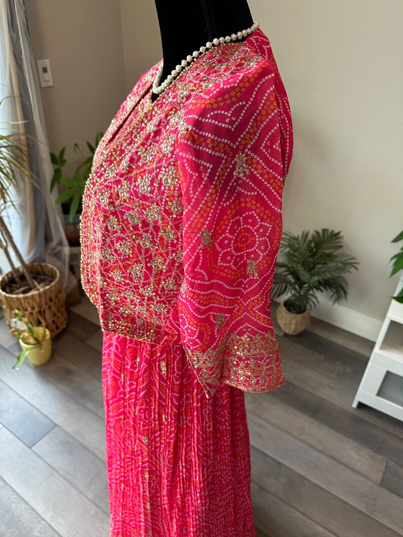 May include: A pink and white patterned dress with gold embroidery and a pearl necklace. The dress has a long skirt and a short-sleeved top.