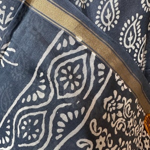 May include: A close-up of a dark blue fabric with a white paisley pattern. The fabric has a gold trim along the edge.