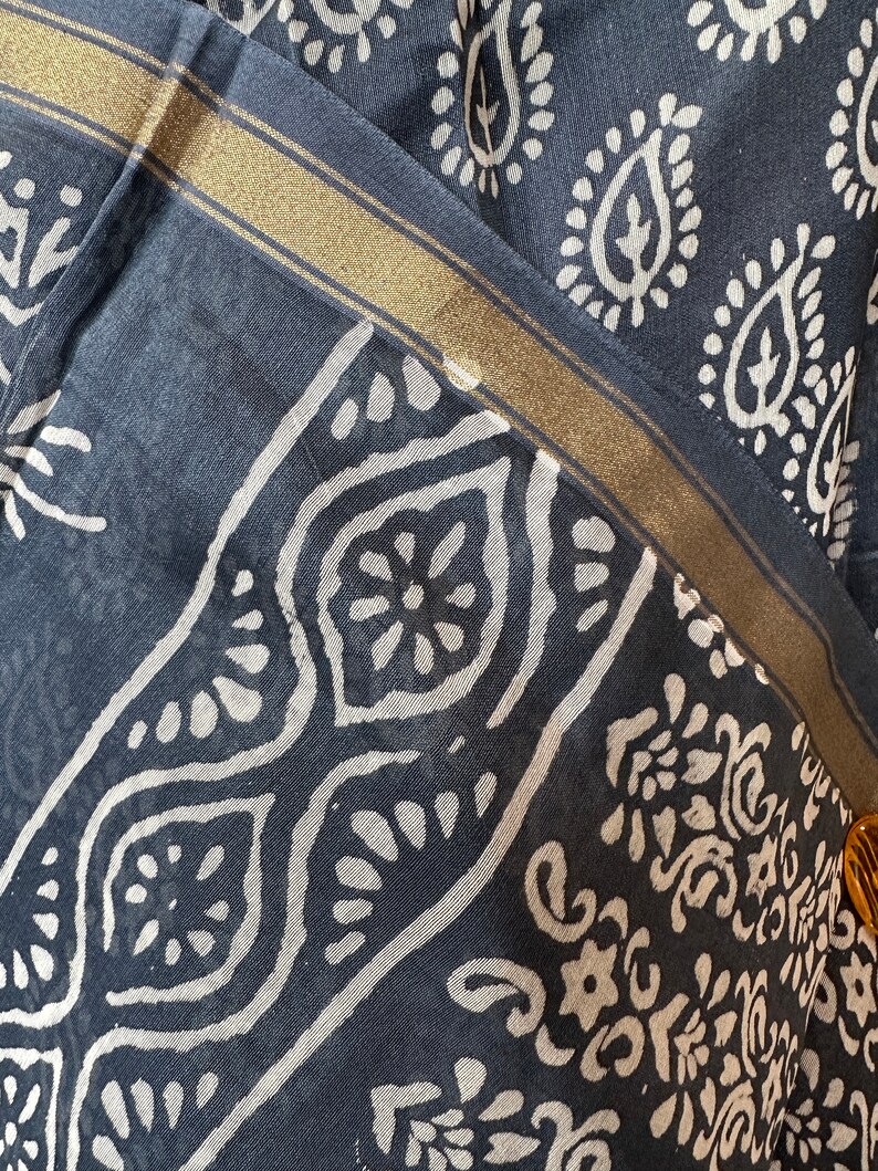 May include: A close-up of a dark blue fabric with a white paisley pattern. The fabric has a gold trim along the edge.
