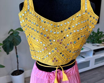 May include: A yellow crop top with mirror embellishments and a pink palazzo pant set. The top has a scoop neck and sleeveless design. The pants have a drawstring waist.
