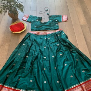 May include: A teal green skirt with a red and gold border. The skirt has a silver floral pattern and is pleated. A matching teal green crop top with silver floral accents is also included.