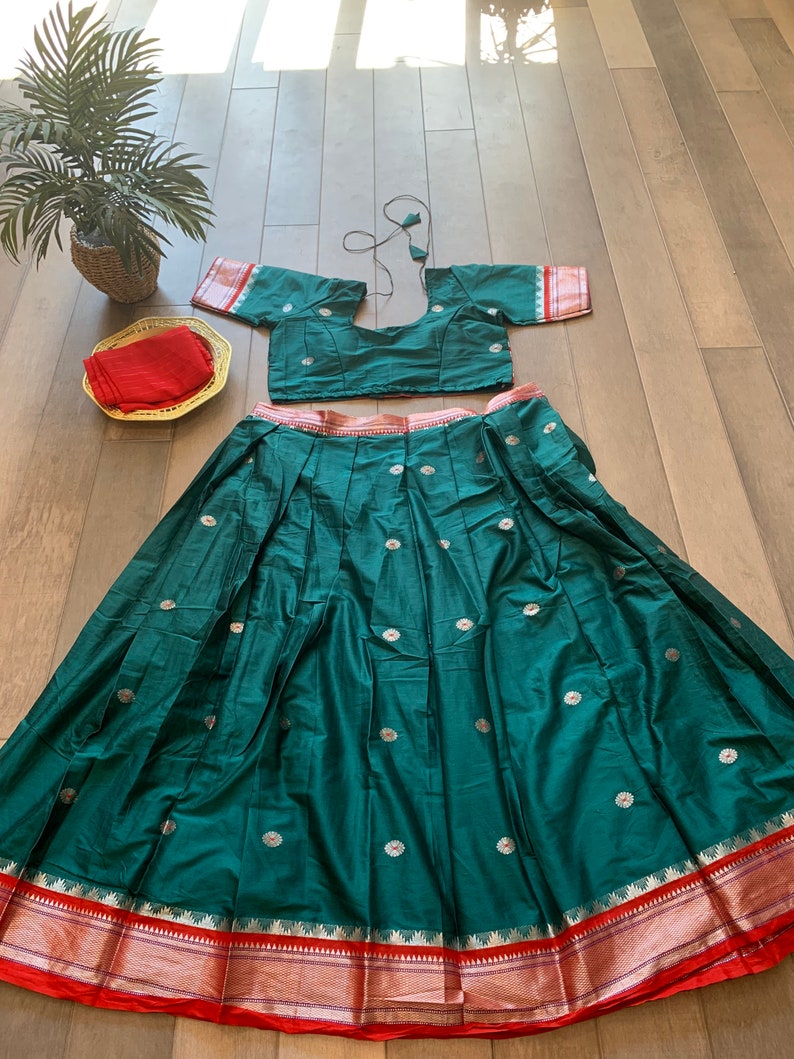 May include: A teal green skirt with a red and gold border. The skirt has a silver floral pattern and is pleated. A matching teal green crop top with silver floral accents is also included.