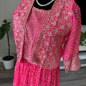 May include: A pink and white dress with gold embroidery and sequins. The dress has a fitted bodice and a flowing skirt. The dress is on a mannequin.