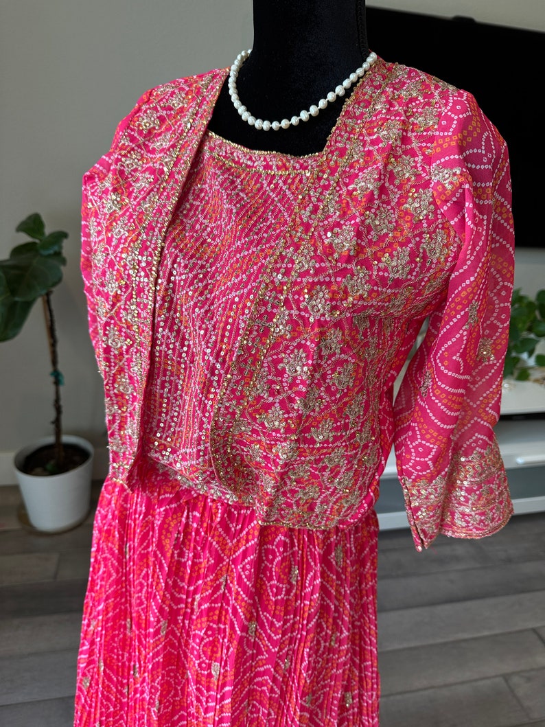 May include: A pink and white dress with gold embroidery and sequins. The dress has a fitted bodice and a flowing skirt. The dress is on a mannequin.