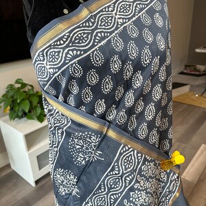 May include: A grey cotton scarf with a white paisley print and gold trim. The scarf is draped over a mannequin.