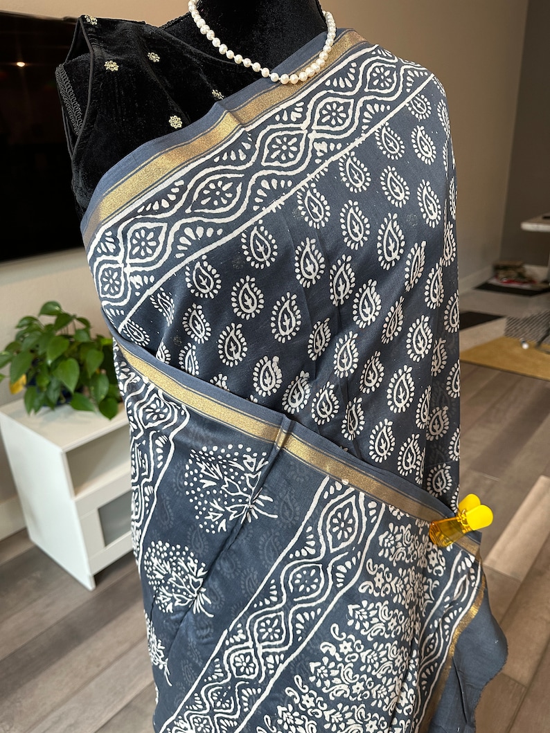 May include: A grey cotton scarf with a white paisley print and gold trim. The scarf is draped over a mannequin.
