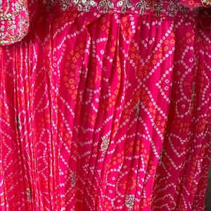 May include: Pink fabric with a white and orange geometric pattern. The fabric is pleated and has silver sequins throughout.