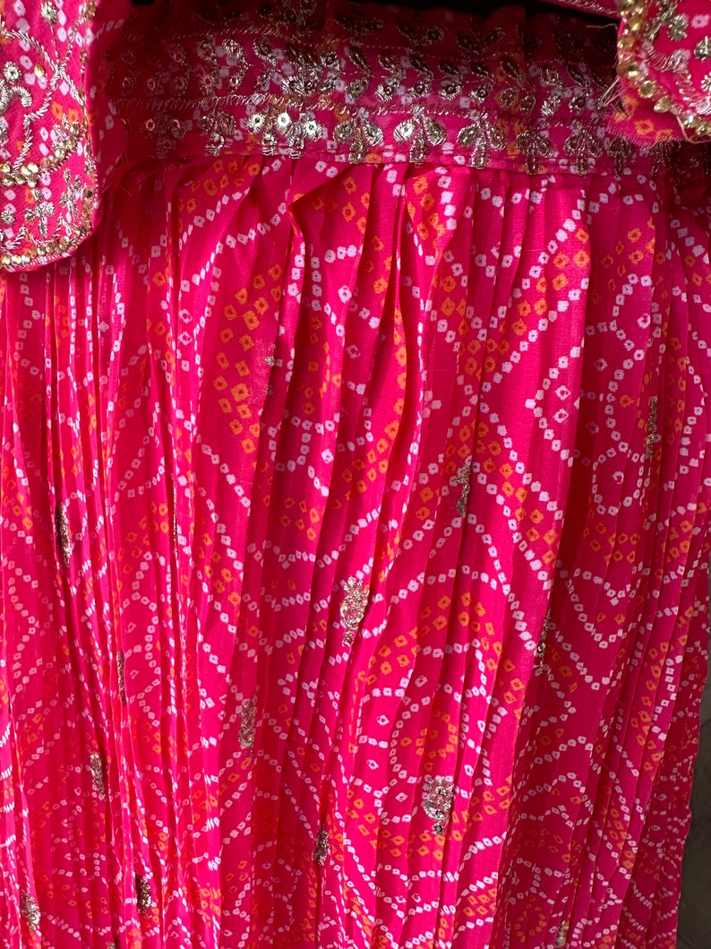 May include: Pink fabric with a white and orange geometric pattern. The fabric is pleated and has silver sequins throughout.