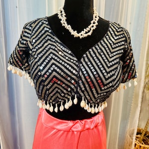 May include: A black sequined crop top with a geometric pattern and white shell trim. The top is paired with a bright pink satin skirt.