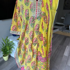 May include: A yellow and pink floral print kurta with a matching dupatta. The kurta has a silver embroidered neckline and the dupatta has a silver border. The kurta is worn over a pink skirt.