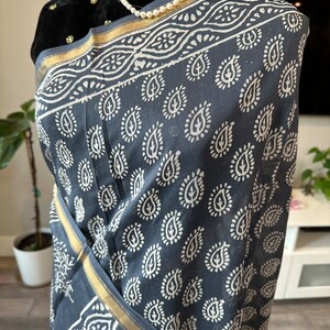 May include: A grey cotton saree with a white paisley print and a gold border. The saree is draped over a mannequin.