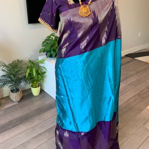 May include: A purple and blue silk saree with gold embroidery and a gold necklace. The saree is draped on a mannequin.