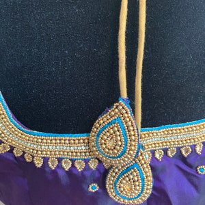 May include: Purple and pink fabric with gold and blue beaded embellishments. The fabric has a satin finish and is decorated with a beaded design around the neckline.