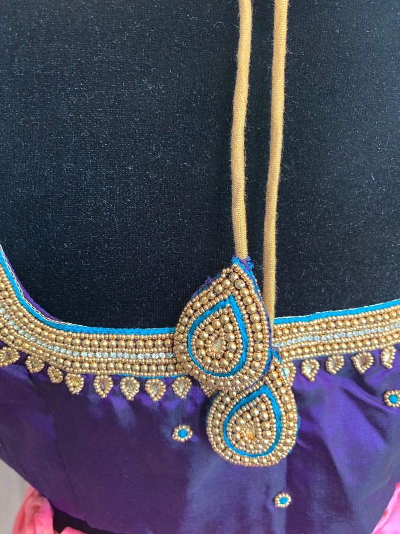 May include: Purple and pink fabric with gold and blue beaded embellishments. The fabric has a satin finish and is decorated with a beaded design around the neckline.