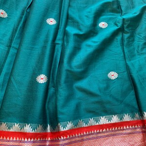 May include: Teal fabric with a silver and red border. The fabric has a repeating pattern of white flowers with red centers.