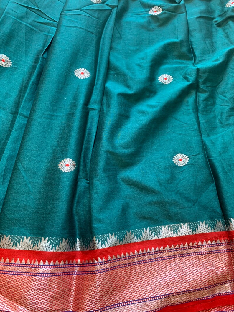 May include: Teal fabric with a silver and red border. The fabric has a repeating pattern of white flowers with red centers.