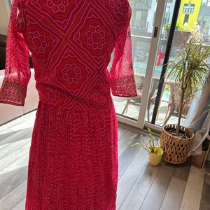May include: A pink and white patterned dress with a long skirt and three-quarter sleeves. The dress has a geometric pattern with small white dots and larger white flowers.