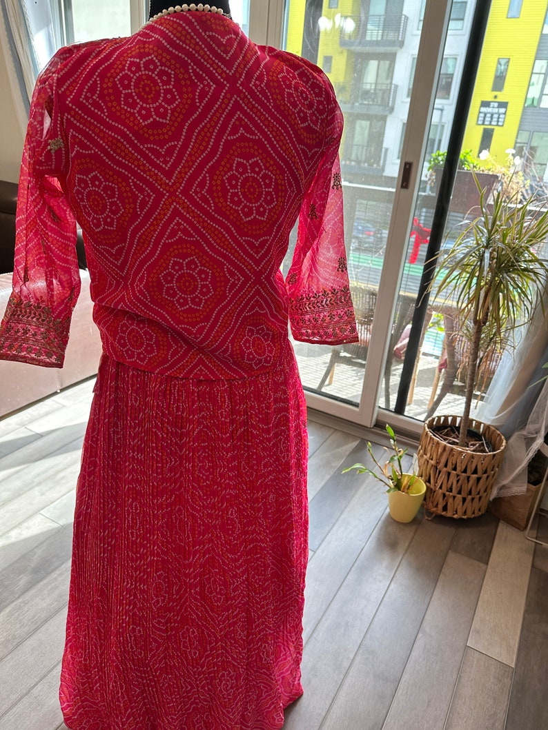 May include: A pink and white patterned dress with a long skirt and three-quarter sleeves. The dress has a geometric pattern with small white dots and larger white flowers.