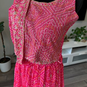May include: A pink and white patterned dress with gold and silver embellishments. The dress has a sleeveless bodice and a flowing skirt.