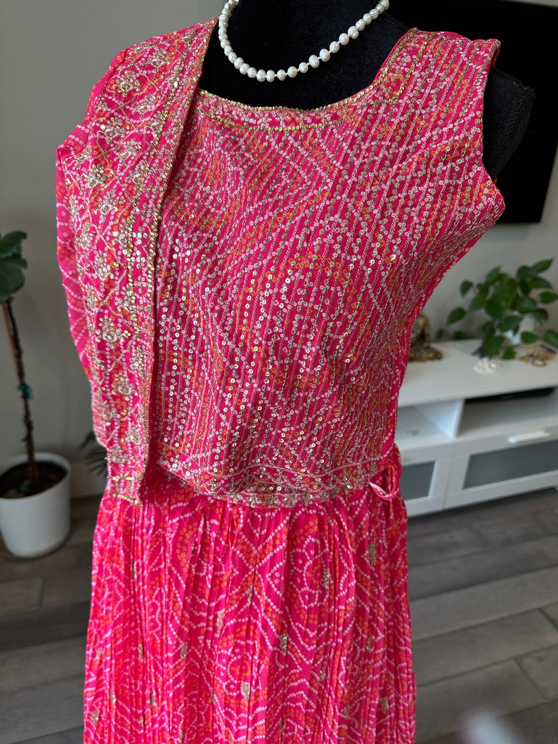 May include: A pink and white patterned dress with gold and silver embellishments. The dress has a sleeveless bodice and a flowing skirt.
