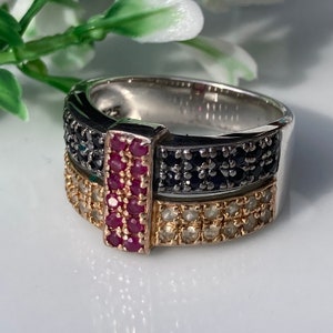 May include: A silver ring with a black and white band and a red ruby stone in the center. The ring is set with small diamonds.