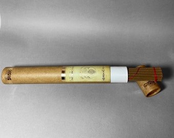 May include: A cylindrical, tan incense container with gold accents and a white label. The incense sticks are visible, bound with a red string, and are accompanied by a decorative incense holder. The background is a solid gray.
