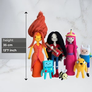 May include: A set of five crocheted plush toys inspired by the animated series Adventure Time. The characters include Finn the Human, Jake the Dog, Princess Bubblegum, Marceline the Vampire Queen, and Flame Princess. The toys are approximately 13.7 inches tall.