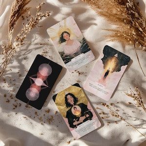 May include: Four tarot cards with illustrations and text are arranged on a white surface with dried plants. The cards feature images of women, geometric shapes, and celestial themes. The cards have titles like "Seethe" and "Purify".
