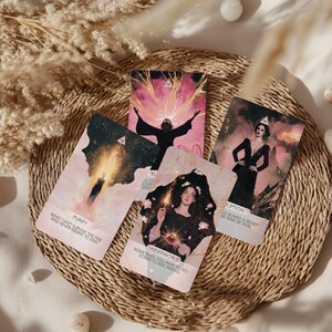 May include: Four tarot cards with illustrations and text, arranged on a woven mat. The cards feature images of figures and symbols in shades of pink, black, and gold. Text on the cards includes "Purify," "Underworld," and "Rupture."