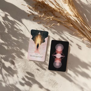 May include: Two tarot cards with celestial designs. One card features a figure in a bright light with the word "PURIFY" and the text "WHAT CAN'T SURVIVE THE FIRE WAS NEVER MEANT TO STAY." The other card has a black background with pink geometric shapes.