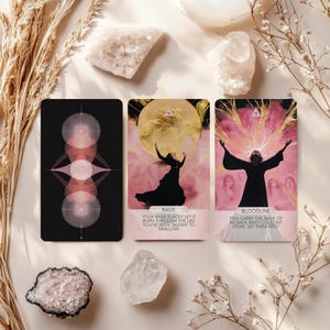 May include: Three tarot cards with illustrations and text, including "RAGE" and "BLOODLINE". The cards are black with pink and white accents. The image includes crystals and dried plants, creating a mystical aesthetic.