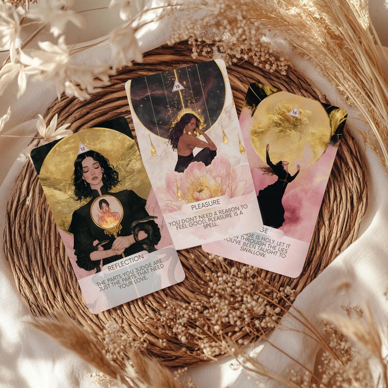May include: Three tarot cards with illustrations and text, arranged on a woven mat with dried floral accents. The cards feature images of women and celestial elements, with phrases like "Reflection" and "Pleasure". The color palette includes gold, pink, and black.