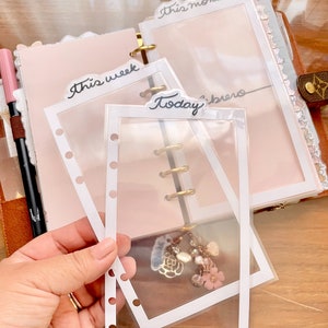 Peut inclure: Trois pochettes en plastique transparent avec des bordures blanches pour un agenda ou un journal. Les pochettes sont &eacute;tiquet&eacute;es "Cette semaine", "Aujourd'hui" et "Ce mois-ci".