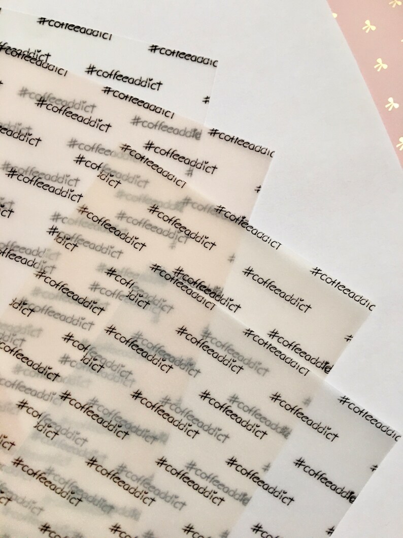 May include: Multiple sheets of translucent paper are printed with the hashtag and word "coffeeaddict" in a repeating pattern. The text is in a simple, sans-serif font and is printed in black ink. The paper has a slight texture.